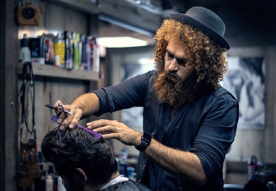 Ein Friseur bei der Arbeit mit einer Schere am Schneiden und sieht dabei auch noch cool aus wenn der Bussiness den Haarschnitt bekommt, ganz genau so wie in userer Topliste der besten Friseure und Barbiere in Köln.