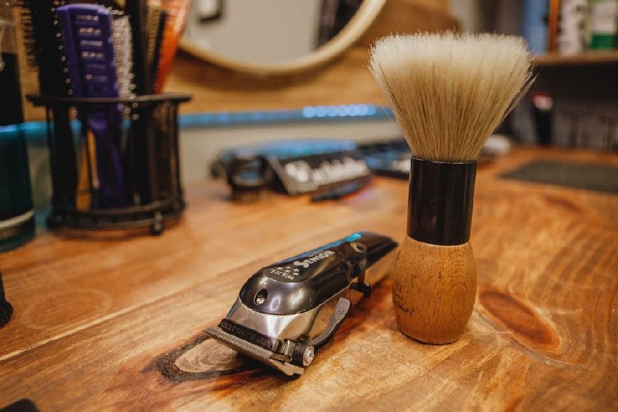 Barbershop with hair clipper and brush and shaving kit on the table in front of the camera lens.
